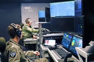 MQ-25 Air Vehicle Pilots Lt. Matt Pence (forward) and Lt. Steven Wilster, conduct test run to monitor the Unmanned Carrier Aviation Mission Control System ground control station, located at Naval Air Station Patuxent River, Md., as the system commands the General Atomics Aeronautical Systems, Inc. (GA-ASI) MQ-20 Avenger surrogate, located at the company’s test facility in California, in preparation for demonstration event in November 2024. (Photo: U.S. Navy)